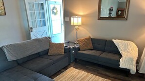 A living room with two grey sofas, a patterned rug, a lamp, and a door with a wreath.