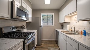 A kitchen with white cabinets, a stainless steel microwave, a stove, and a dishwasher.