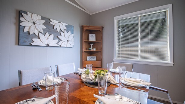 A dining room with a wooden table set for four, a floral wall art piece, and a window with blinds.