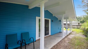 A blue house with a covered porch, a sliding glass door, and two chairs.