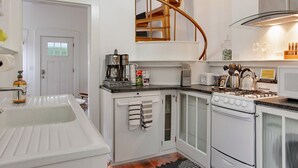 Eine moderne Küche mit weißen Schränken, einem eingebauten Herd, einer Kaffeemaschine und einer Wendeltreppe.