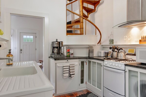 A modern kitchen with white cabinetry, a built-in stove, a coffee maker, and a spiral staircase.
