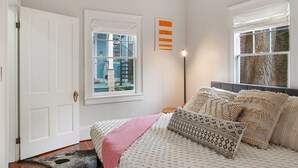 Ein Schlafzimmer mit einem Bett, einem Fenster mit Blick auf ein blaues Gebäude, einer Stehlampe und einer Tür.