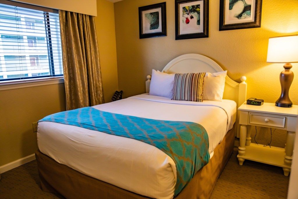 A hotel room with a bed, a nightstand, a lamp, and a window with curtains.