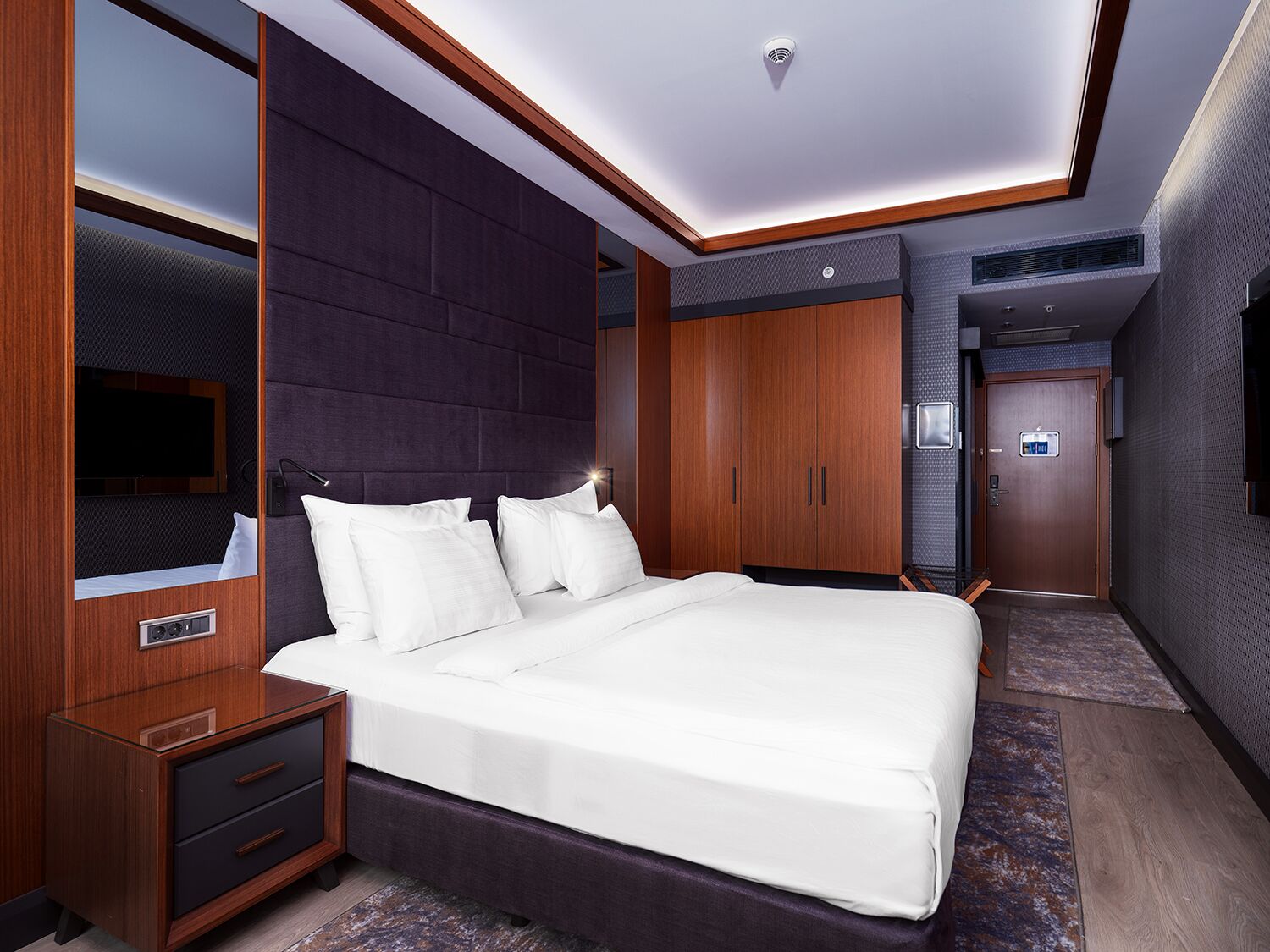 Ein modernes Hotelzimmer mit einem großen Bett, einem Holzschrank und einem Fernseher.