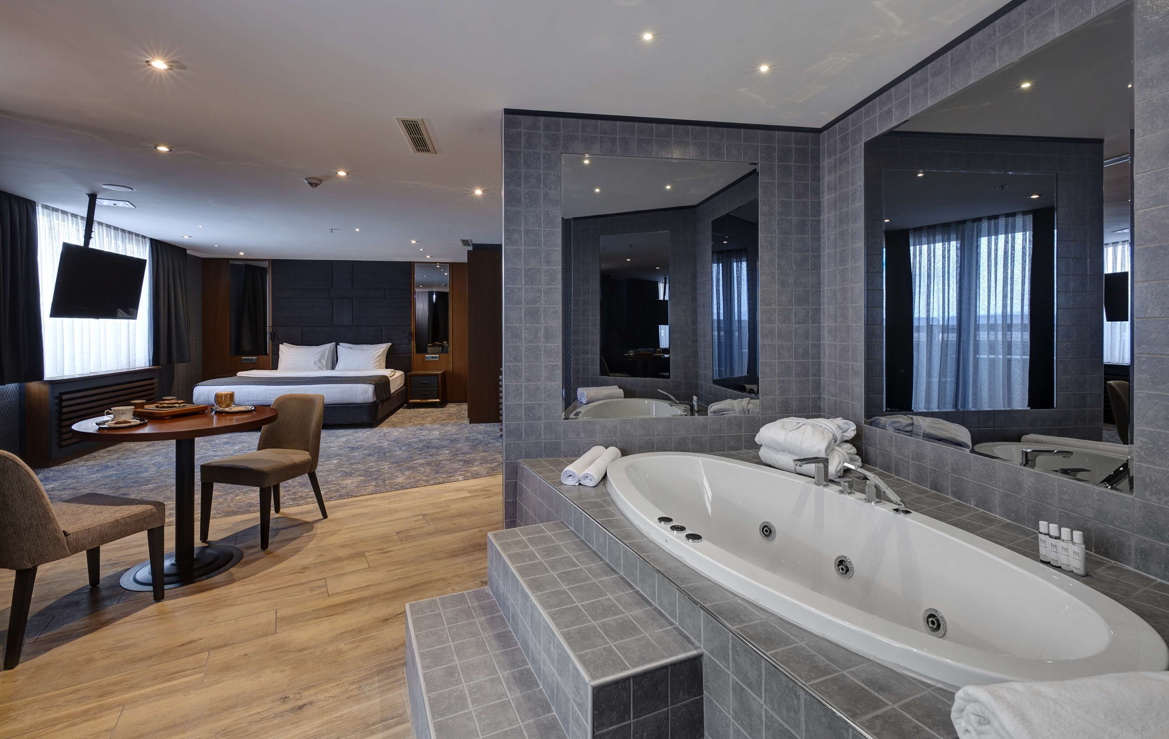 Une chambre d’hôtel moderne dotée d’un grand lit, d’un coin salon avec une table et des chaises, d’une grande baignoire et d’un grand miroir.