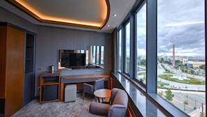 Une chambre d’hôtel moderne dotée d’une grande fenêtre, d’un téléviseur à écran plat, d’un bureau et d’un coin salon.