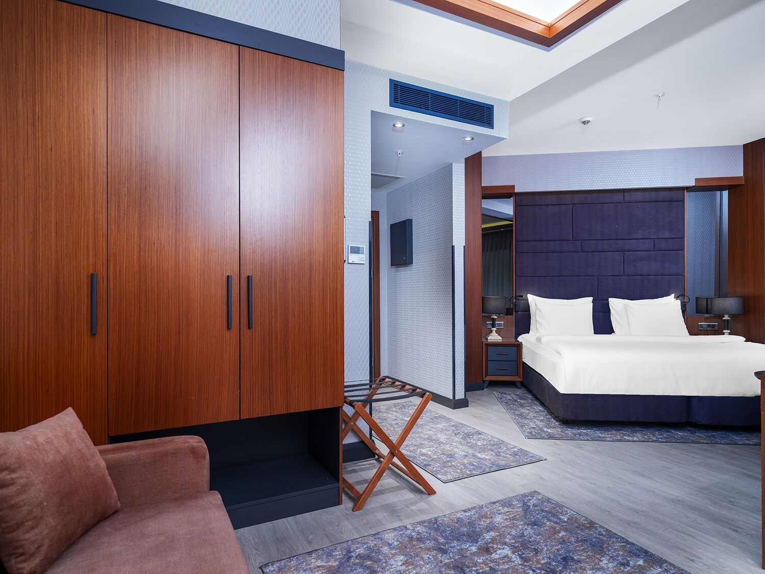 A modern hotel room with a large wardrobe, a bed with white linens, and a small bedside table.