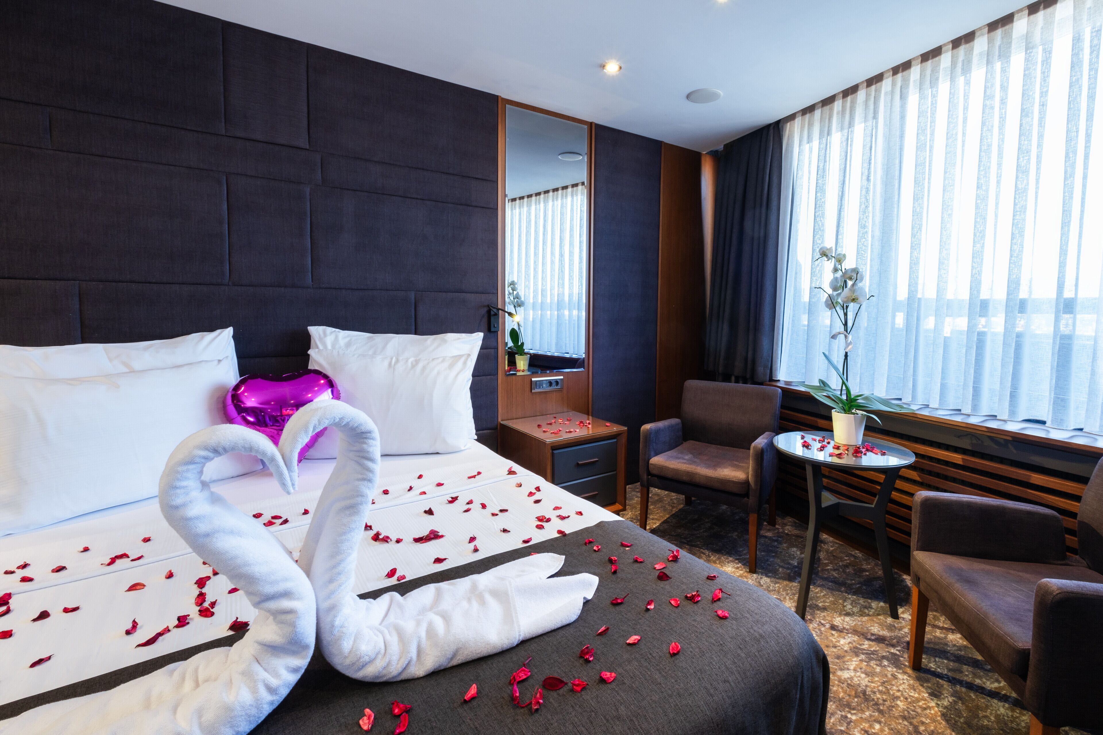 A hotel room with a large bed, a desk, a chair, and a window with curtains.