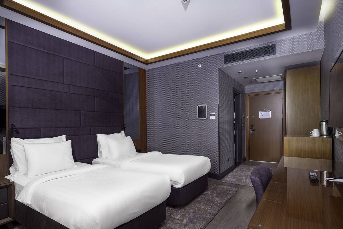 A modern hotel room with two beds, a desk, and a bathroom.