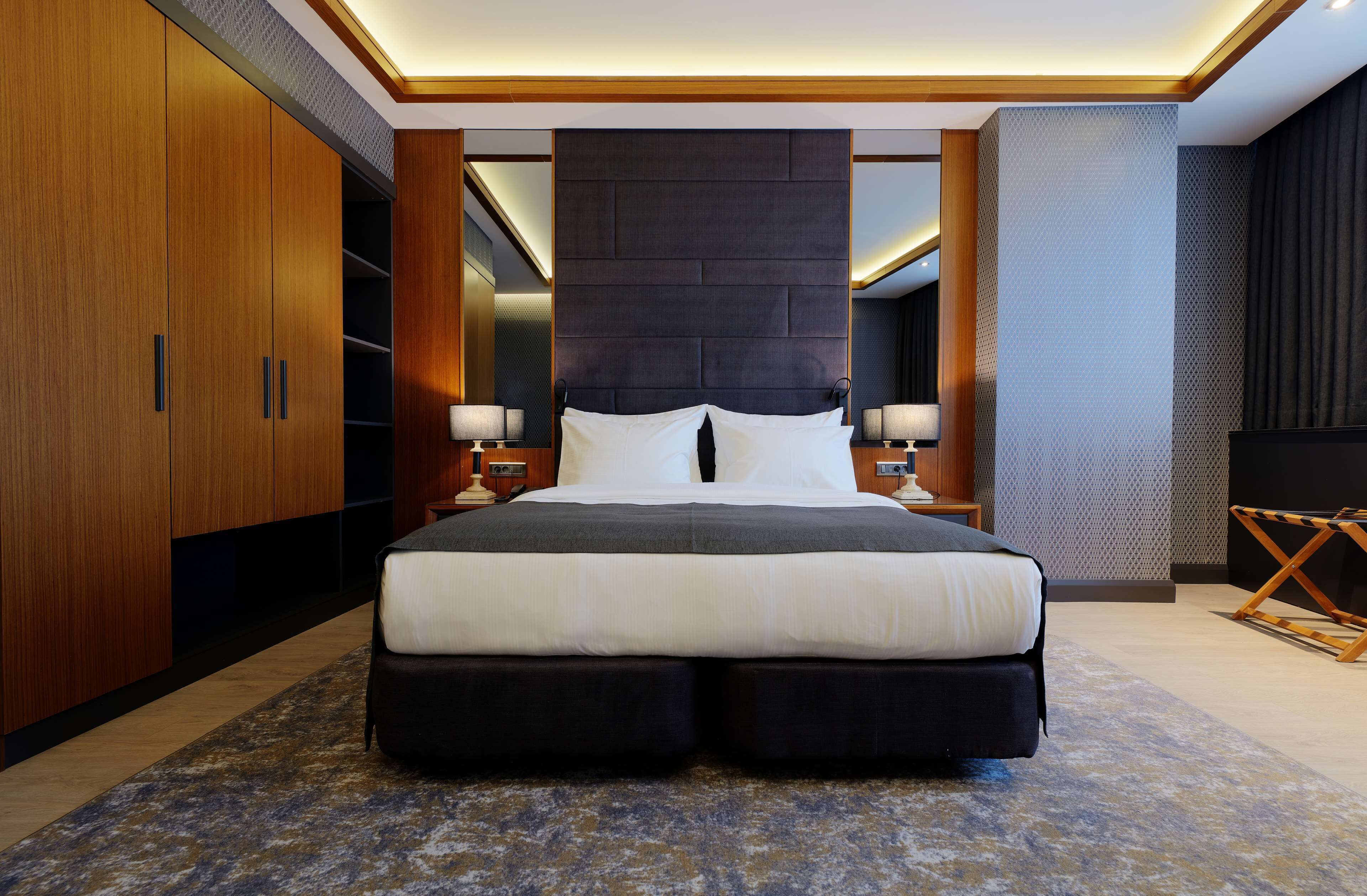 Une chambre d’hôtel moderne avec un grand lit, une armoire en bois et une tête de lit sombre.
