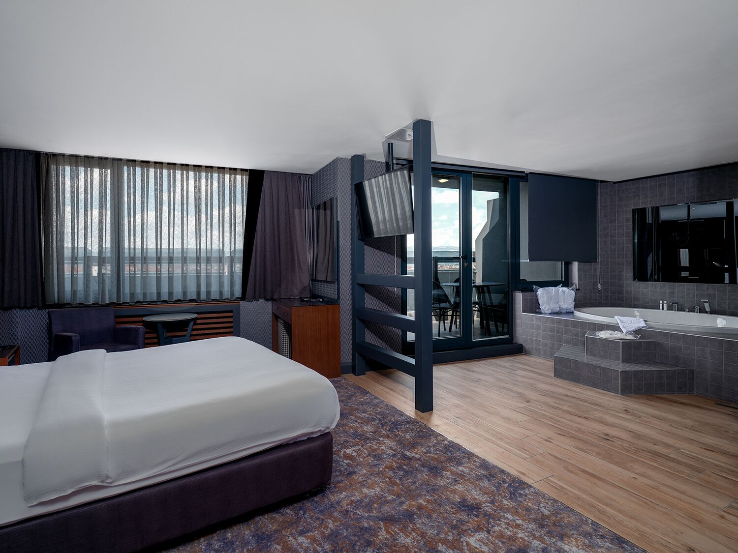Ein modernes Hotelzimmer mit einem großen Bett, einem Schreibtisch, einem Balkon und einem Badezimmer.