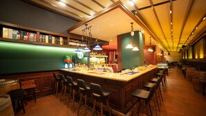Un espace bar doté d’un long comptoir, de nombreux tabourets et d’étagères remplies de bouteilles.