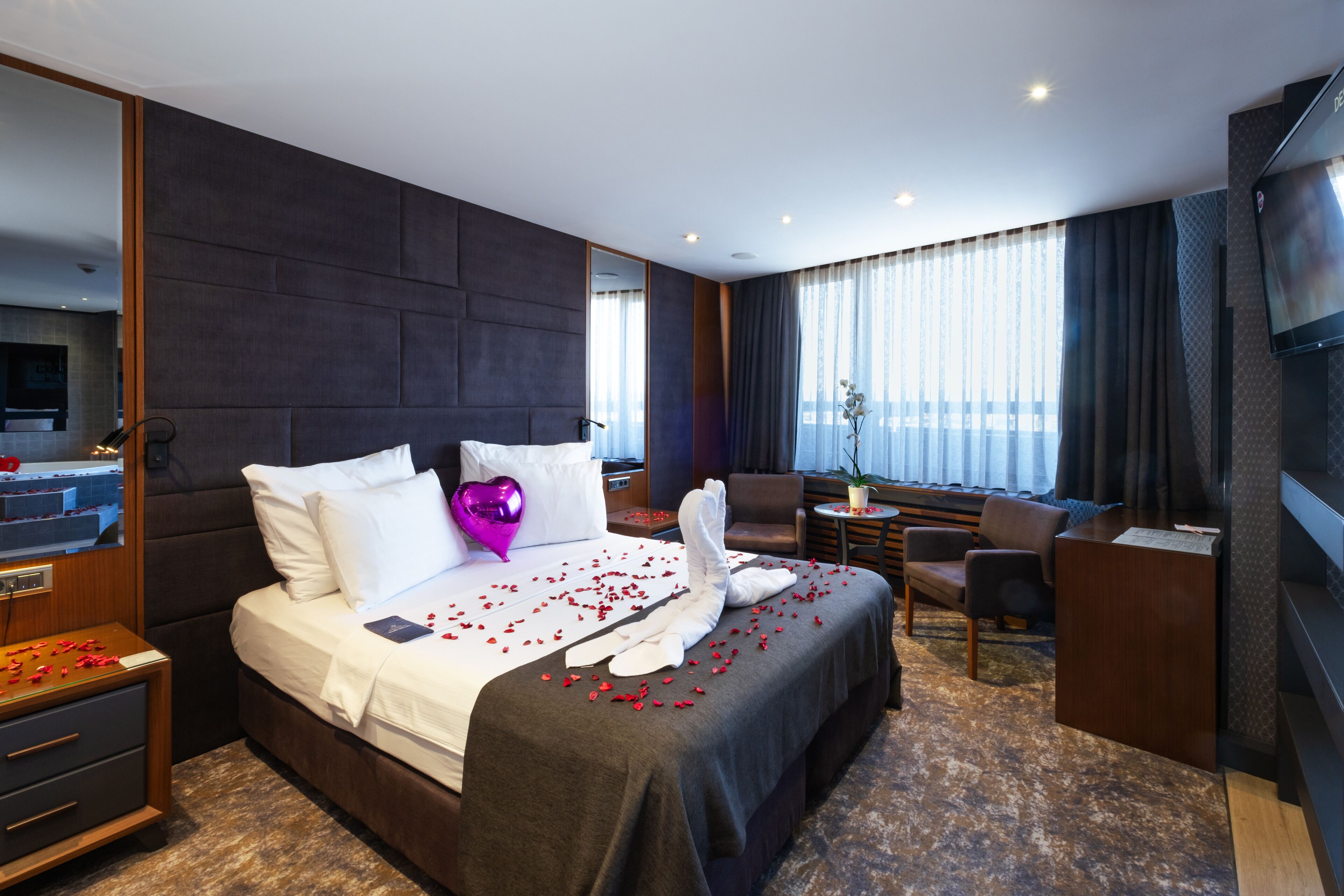 A hotel room with a large bed, a desk, a chair, and a TV.