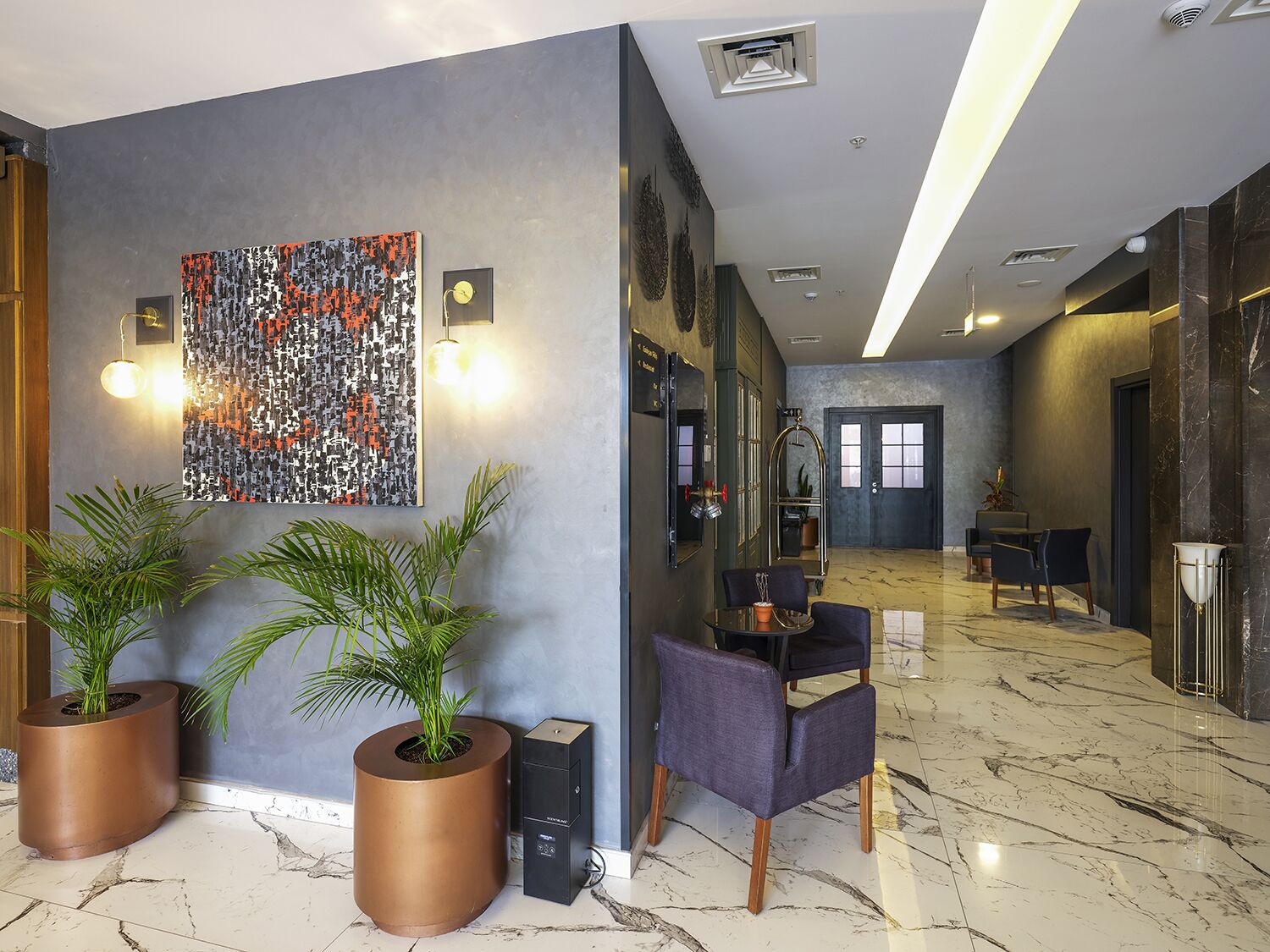 Eine moderne Lobby mit einem großen abstrakten Kunstwerk, zwei topfgepflanzten Pflanzen, einer Sitzecke mit Stühlen und einem Marmorboden.