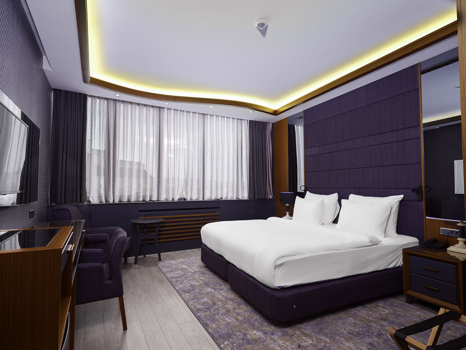 A modern hotel room with a large bed, a desk, and a seating area.