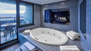 Une salle de bain moderne dotée d’une grande baignoire, d’un espace détente clos par des parois de verre et offrant une vue sur la ville.