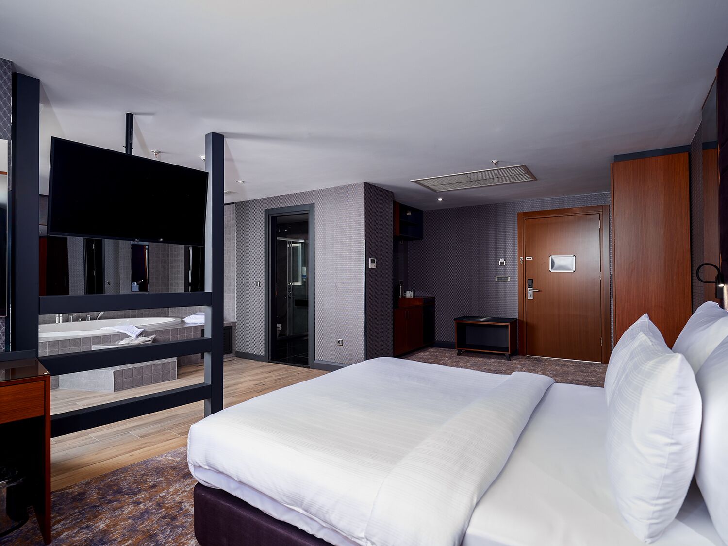 A modern hotel room with a large bed, a TV, a desk, and a bathroom with a shower and toilet.