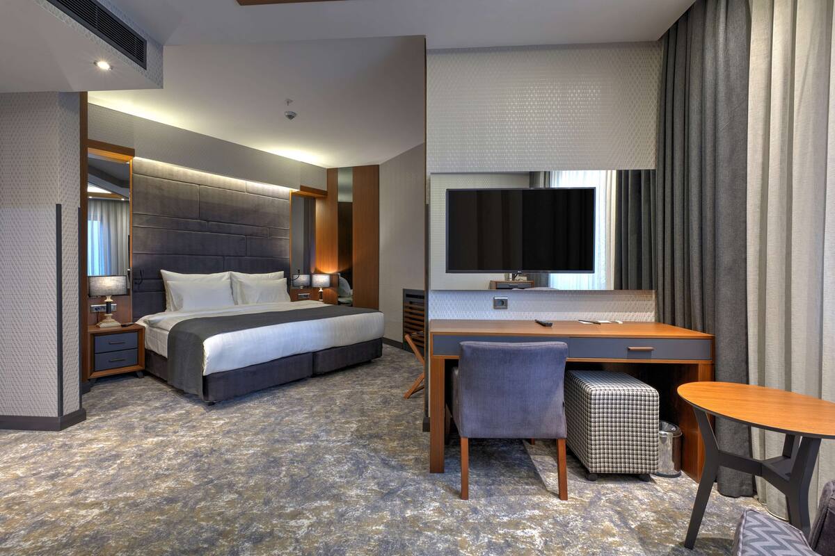 A hotel room with a large bed, a desk with a chair, a television, and a window with curtains.