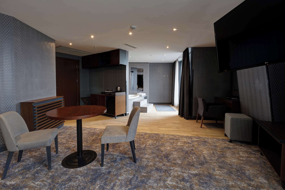 A modern living room with a round table, two chairs, a sofa, and a TV.