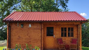 Une cabane en bois avec un toit recouvert de tuiles rouges, une porte d’entrée et deux fenêtres.