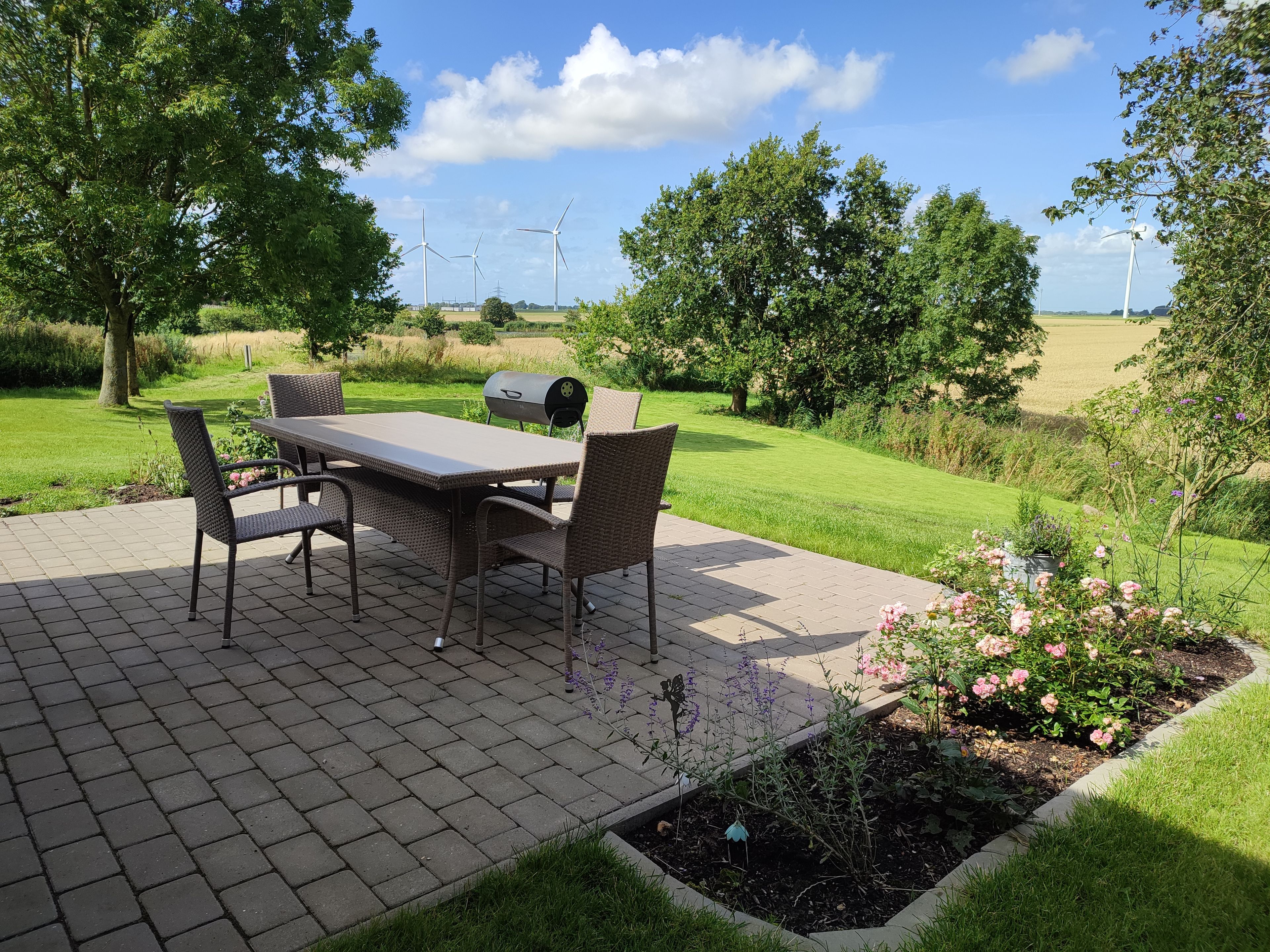 An outdoor patio with a table and chairs, surrounded by a garden with flowers and grass.