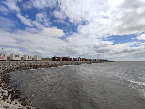 Una hilera de cabañas de playa a lo largo de una costa rocosa, con el mar al fondo.