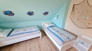 Une chambre avec deux lits simples, une petite table de chevet blanche, une lampe fixée au mur et une décoration en forme de filet.