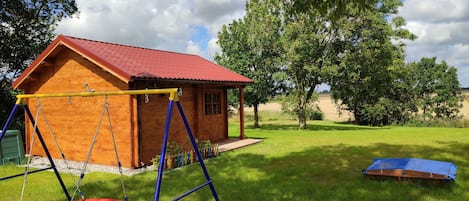A wooden playhouse with a red roof and swing set in a grassy yard.