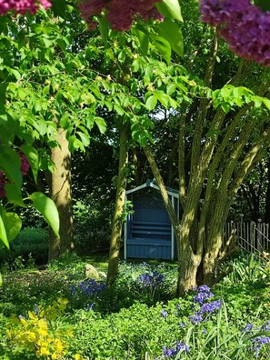 Un jardín con una estructura de madera, rodeado de árboles y plantas en flor.