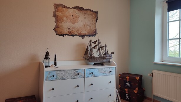 Une pièce avec une commode blanche, une maquette de bateau, une carte et une fenêtre.