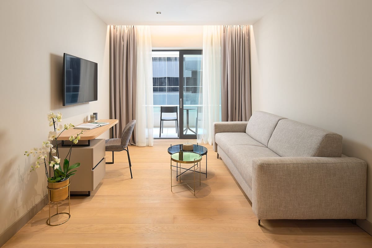 Ein modernes Wohnzimmer mit einer Couch, einem kleinen Tisch, einem Fernseher und einem Schreibtisch mit Stuhl.