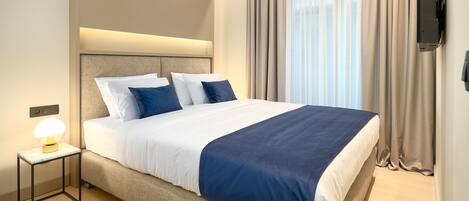 A neatly made bed with a headboard, a bedside lamp, and a flat-screen TV mounted on the wall.