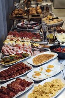 Buffet com diversos alimentos, incluindo carnes, queijos e doces.