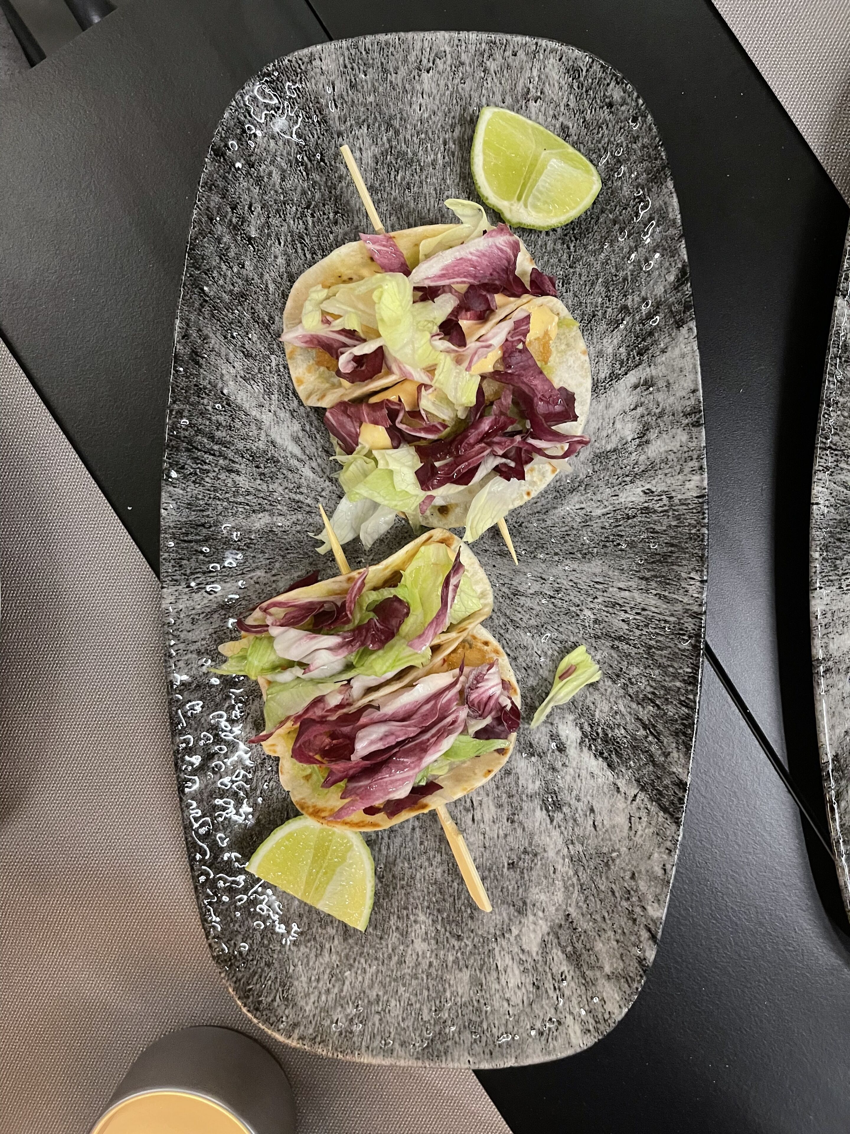 A plate with three tacos on a textured black plate, accompanied by a lime wedge.