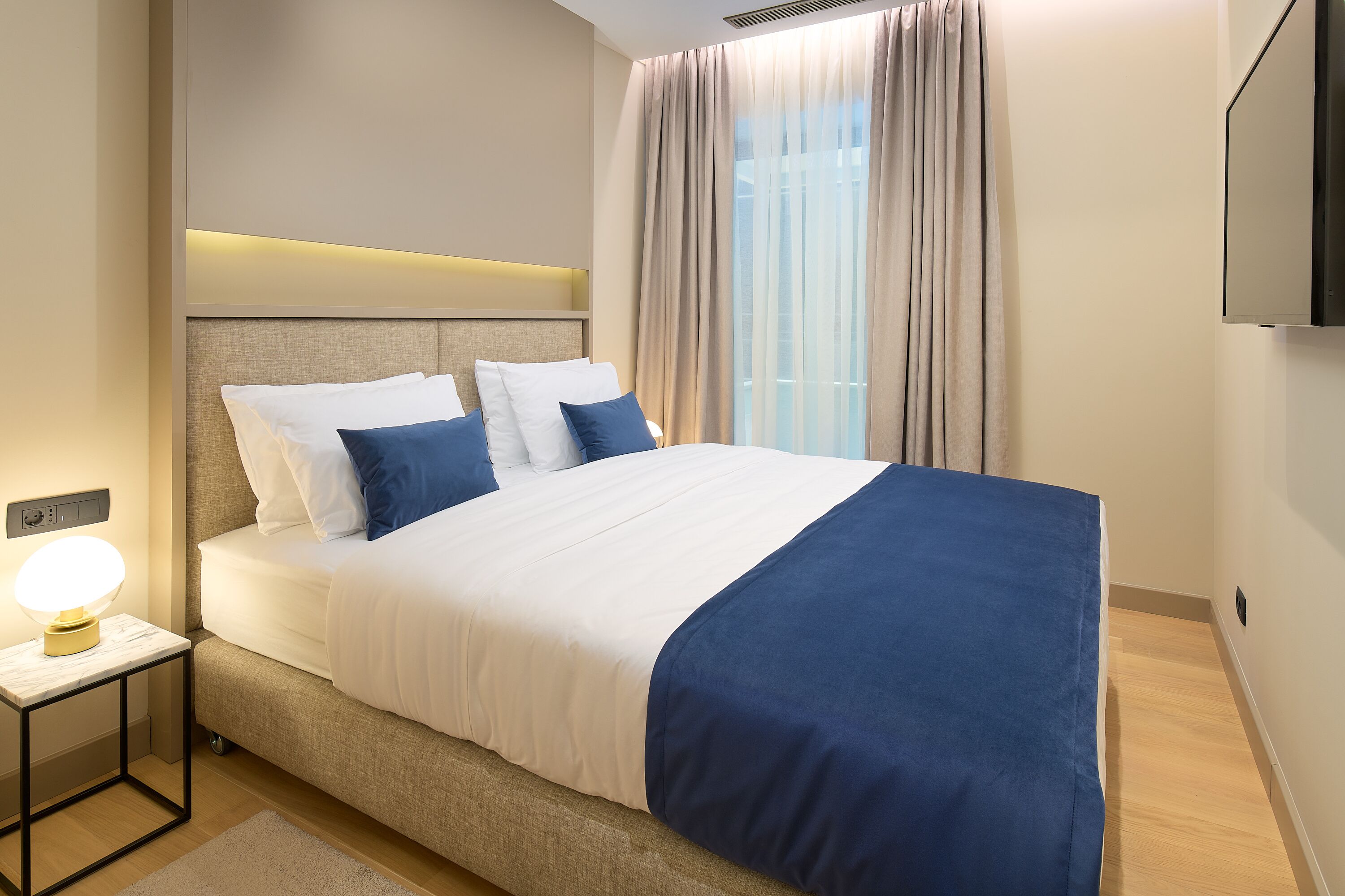 Une chambre d’hôtel moderne avec un grand lit, une table de chevet avec une lampe et un téléviseur fixé au mur.