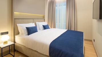 A modern hotel room with a large bed, a bedside table with a lamp, and a TV mounted on the wall.