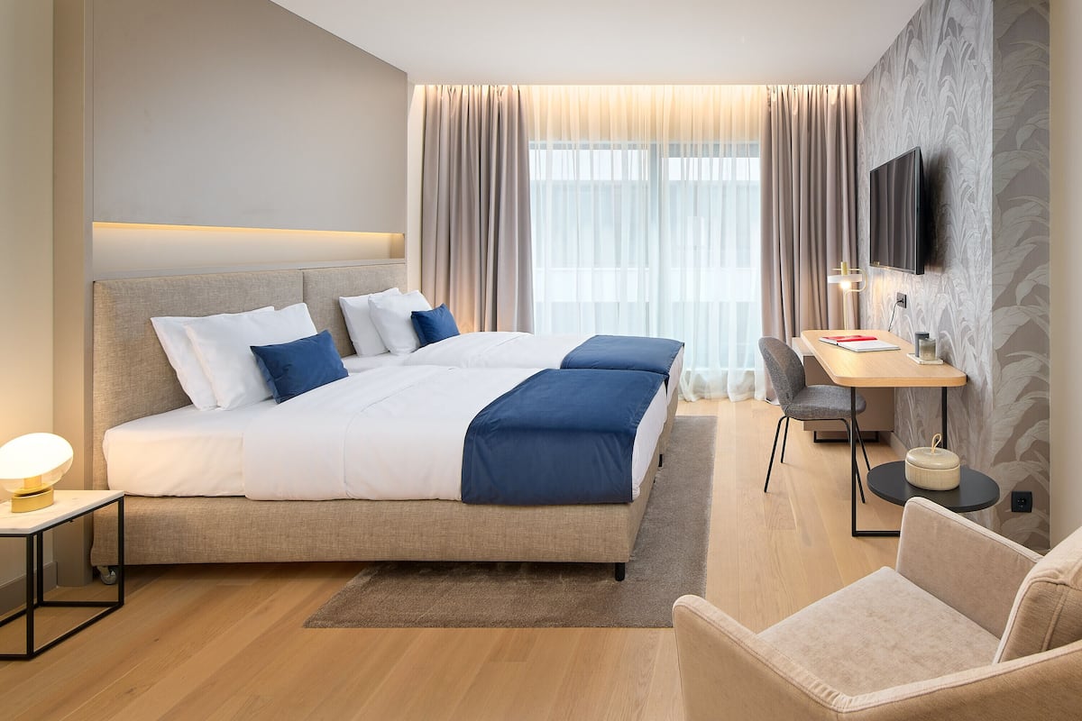 Ein modernes Hotelzimmer mit einem großen Bett, einem Schreibtisch, einem Sessel und einem Fernseher.