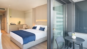 Ein modernes Hotelzimmer mit einem großen Bett, einem kleinen Tisch mit Stühlen, einer Küchenzeile und einem Balkon mit einer Glastür.