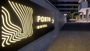 Ein Hotel Eingang mit einem modernen Schild, das den Namen "PORTO HOTEL" und ein stilisierte Flügel-Design zeigt.