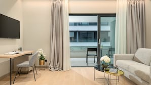 Ein modernes Wohnzimmer mit Schreibtisch, Sofa, Sessel und einer Glastür, die auf einen Balkon führt.