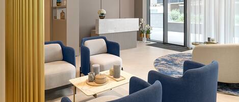 A modern reception area with a marble reception desk, blue upholstered chairs, and a large window offering a view of the outdoors.