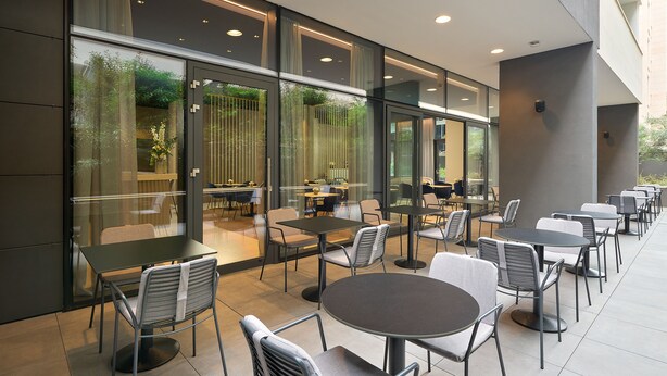 Ein Straßencafé mit Tischen, Stühlen, großen Fenstern und moderner Architektur.