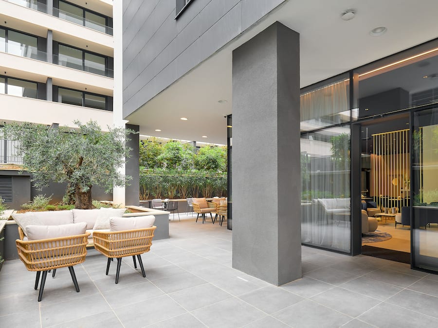 Un patio interior moderno con mobiliario de mimbre, un muro de cristal y vistas del interior.