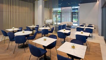 A modern dining area with round tables and blue chairs, featuring a herringbone wood floor and a view of the outdoors.