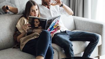 Un couple est assis sur un canapé gris, avec un magazine, une télécommande et une table basse noire à proximité.