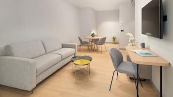A modern living room with a grey sofa, a round coffee table, and a dining area with a small table and chairs.