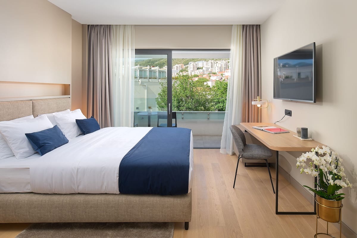 Ein Hotelzimmer mit Bett, Schreibtisch, Sessel, Fernseher und Blick auf die Stadt.