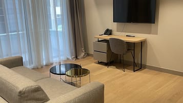 A modern hotel room with a sofa, a desk, a TV, and a small round table.