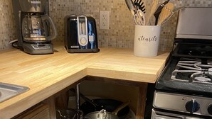 A kitchen with a coffee maker, toaster, utensils holder, stove, and various pots and pans.
